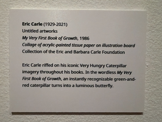 photo of gallery label: “Eric Carle (1929-2021) Untitled artworks My Very First Book of Growth, 1986 Collage of acrylic-painted tissue paper on illustration board Collection of the Eric and Barbara Carle Foundation Eric Carle riffed on his iconic Very Hungry Caterpillar imagery throughout his books. In the wordless My Very First Book of Growth, an instantly recognizable green-and-red caterpillar turns into a luminous butterfly.”