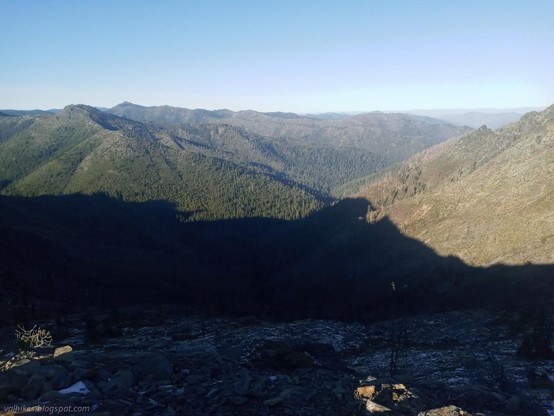 Shadows stretching across a valley toward the Butte Fork Applegate River.

Rocks nearby drop to green below. More green ridges stretch away on the far side of the valley.